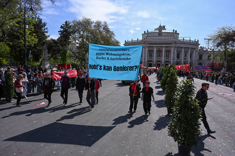 Aktivist*innen halten auf dem SPÖ Maiaufmarsch ein Hochbanner mit der Aufschrift: Sozial treffsicher gegen Wohnungslose, Kinder & Suchtkranke - Hobt's kan Genierer?!